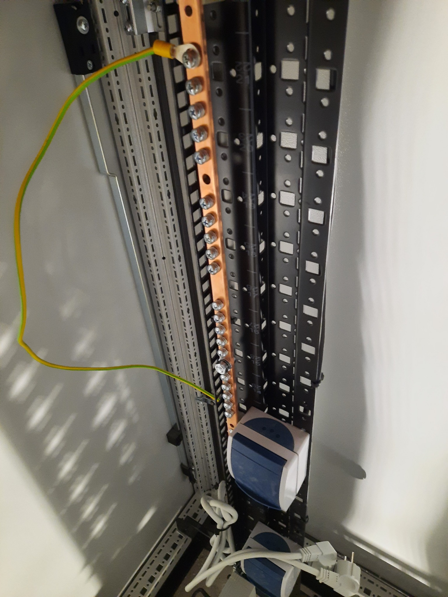 Szyna wyrównawcza potencjałów z podłączonym przewodem ochronnym żółto-zielonym w szafie elektrycznej, widoczne elementy montażowe i przewody zasilające.