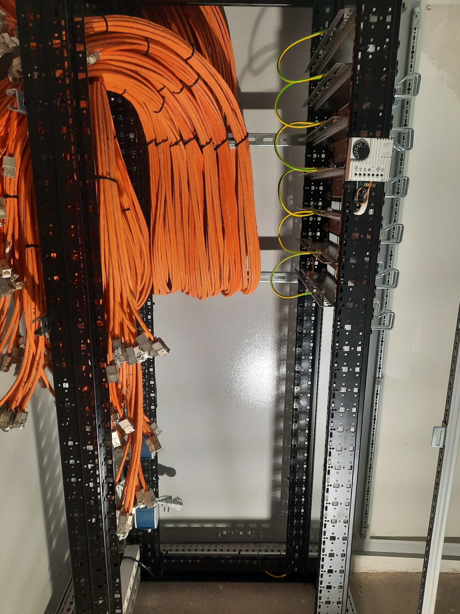Pomarańczowe kable sieciowe uporządkowane w szafie rack, z widocznymi złączami i przewodami uziemiającymi.