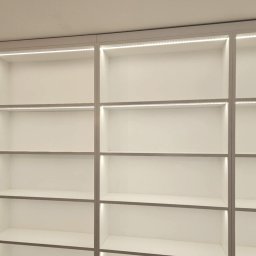 EXPO Kawałkowski Krzysztof - Biała, minimalistyczna szafa wnękowa z oświetleniem LED, prezentująca puste półki i czyste linie. Nowoczesne rozwiązanie do przechowywania.