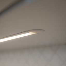 EXPO Kawałkowski Krzysztof - Detal minimalistycznej lampy LED podszafkowej, emitującej ciepłe, jasne światło. Widoczne delikatne wzory na ścianie w tle, podkreślające nowoczesny design.