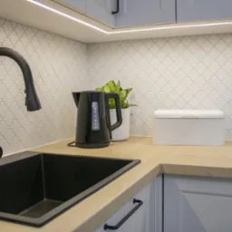 Nowoczesna kuchnia: czarny zlew, bateria, drewniany blat i białe płytki mozaikowe. Oświetlenie LED podkreśla detale.