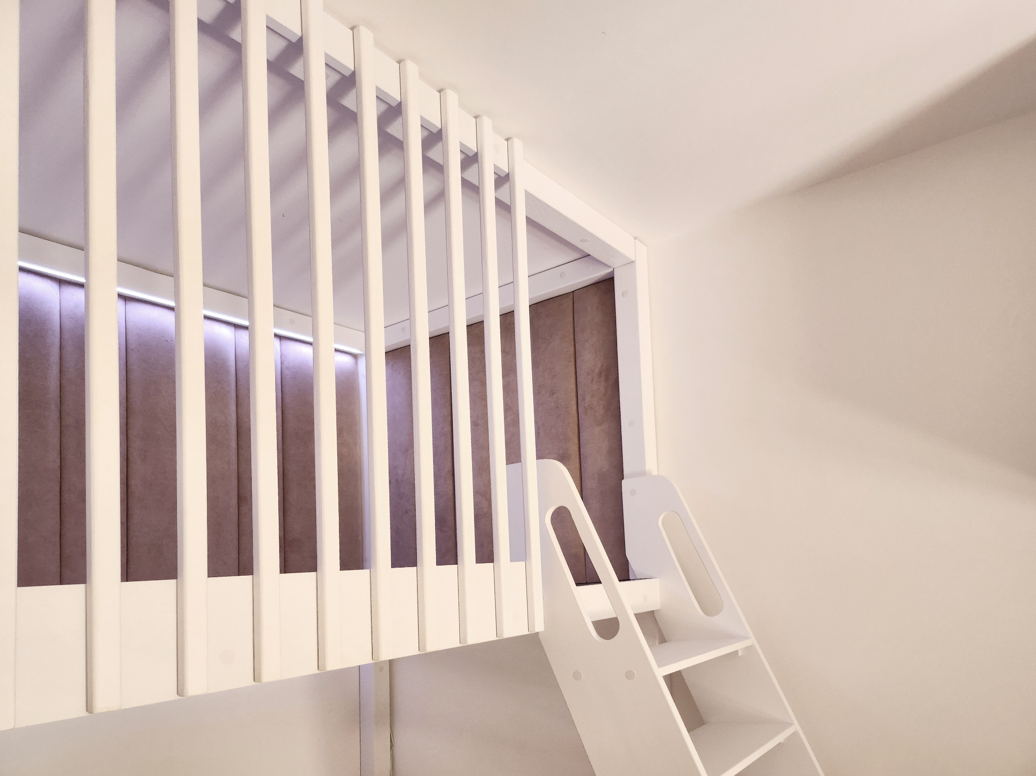 Białe, drewniane łóżko piętrowe z drabinką, zintegrowane z tapicerowanym panelem ściennym w pokoju dziecięcym. Nowoczesny design, minimalistyczny styl.