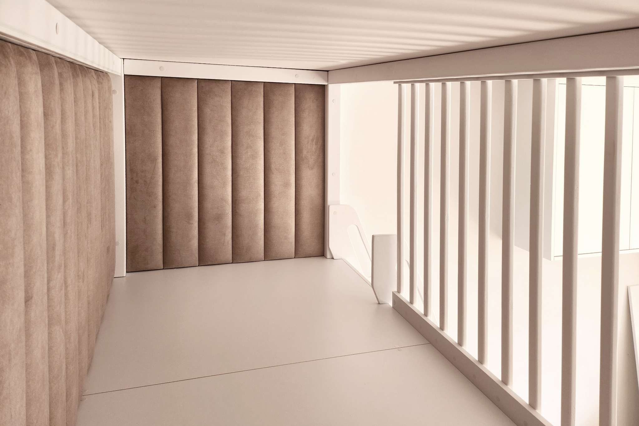 Białe schody z drewnianą balustradą i miękkim, pionowo żłobionym panelem ściennym w odcieniach beżu, tworzące minimalistyczną przestrzeń.