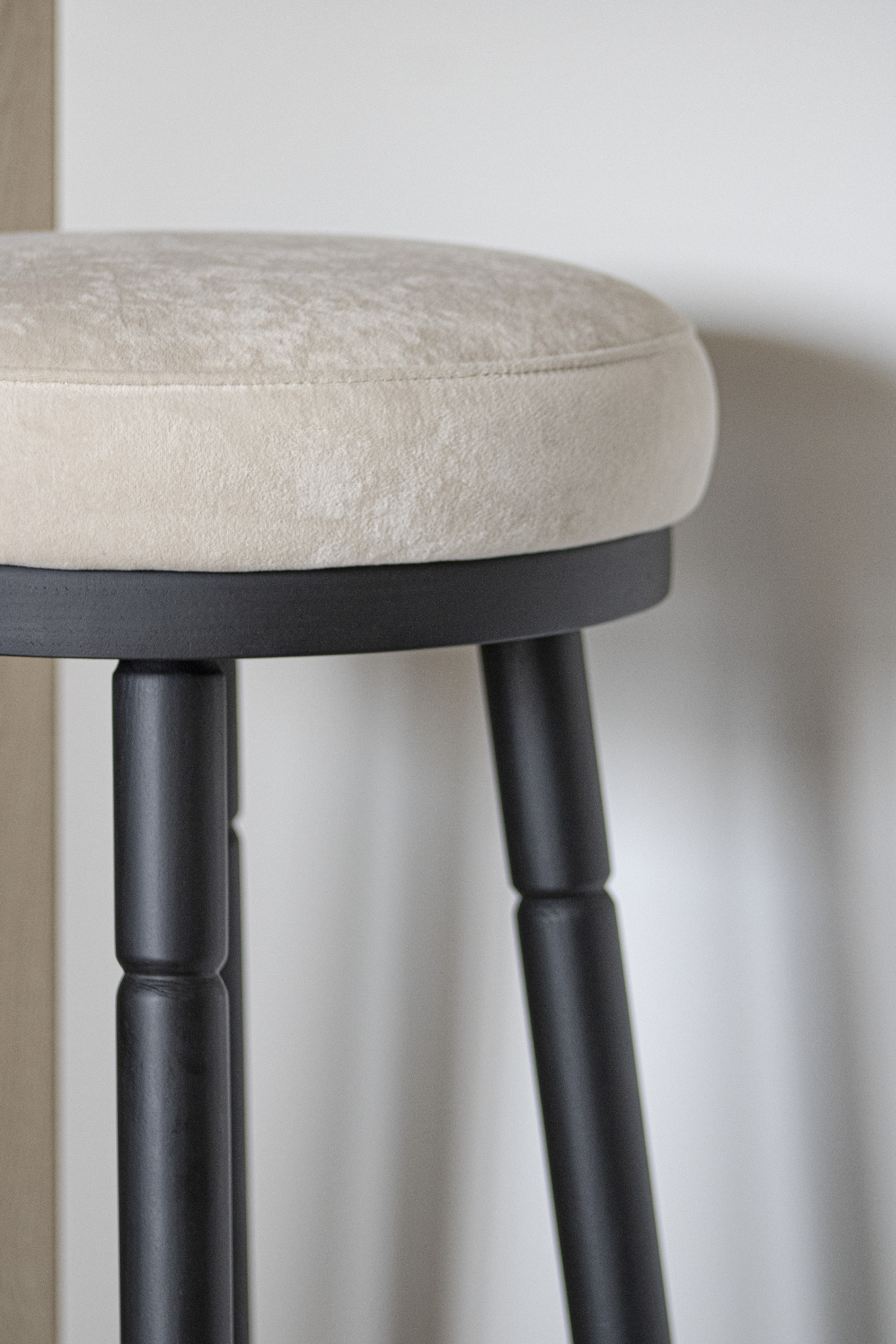 Detale tapicerowanego stołka barowego z ciemnymi nogami, na tle jasnej ściany. Widoczny fragment siedziska i nogi stołka.