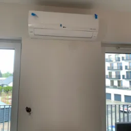 Nowy, biały klimatyzator LG Dual Inverter, jeszcze z folią ochronną i niebieską taśmą, zamontowany na ścianie w jasnym pokoju z widokiem na osiedle, widoczne wystające kable elektryczne.