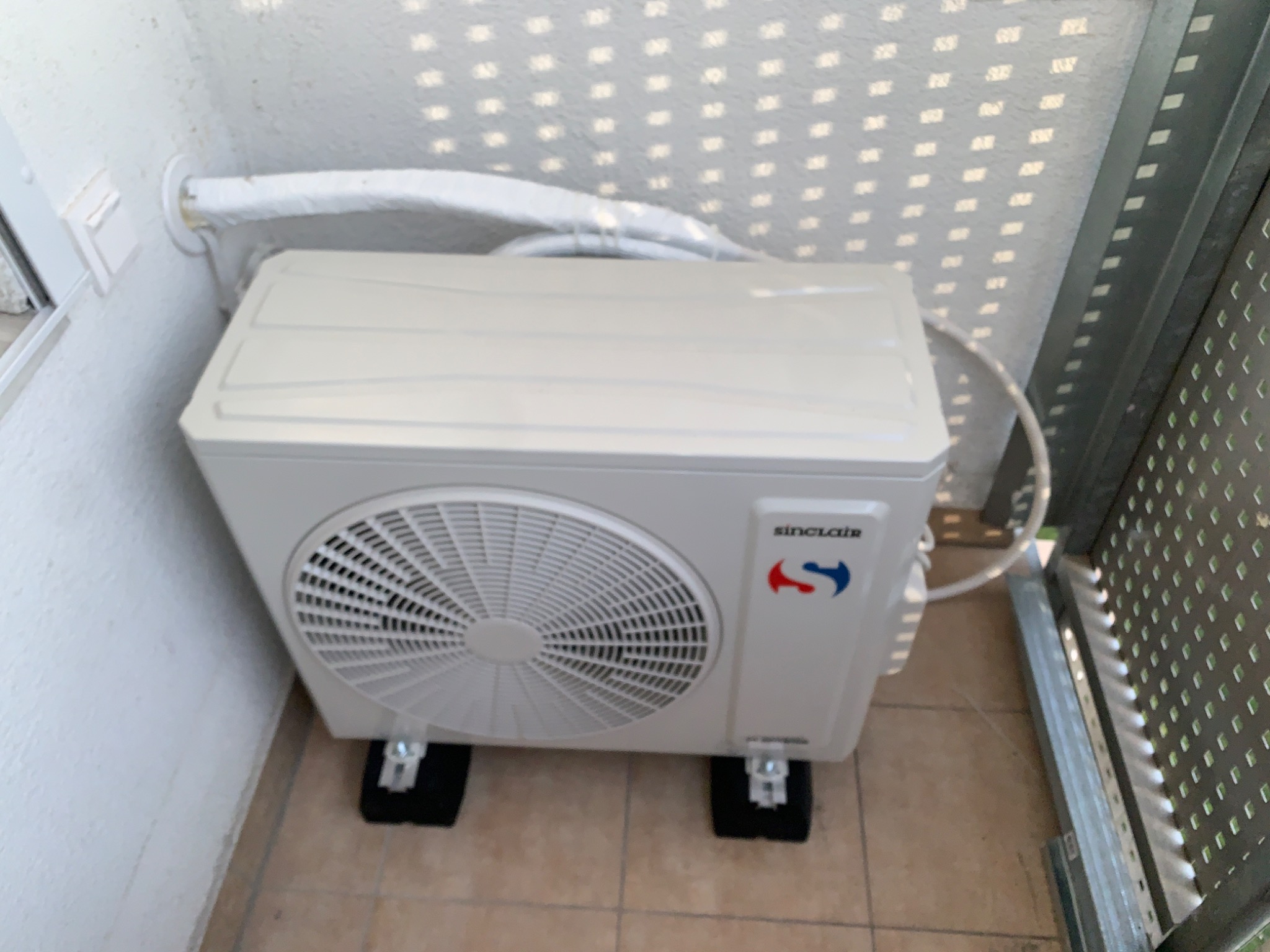 Zewnętrzna jednostka klimatyzacji Sinclair na balkonie, widoczne przewody w izolacji i czarne podkładki pod urządzeniem.