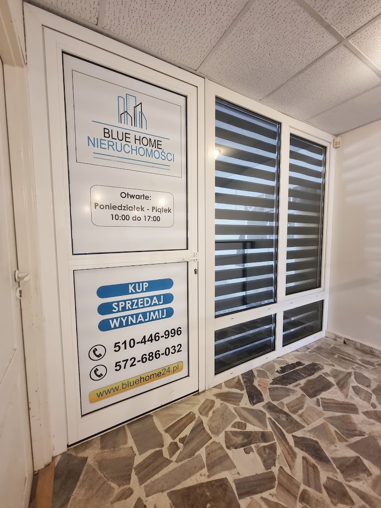 Wejście do biura nieruchomości Blue Home z informacją o godzinach otwarcia, numerami telefonów i adresem strony internetowej, na drzwiach naklejki informujące o kupnie, sprzedaży i wynajmie...