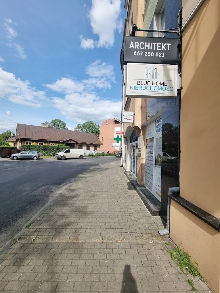 Zewnętrzny widok biura nieruchomości Blue Home z szyldem i numerem telefonu, umieszczonego na rogu budynku przy chodniku z kostki brukowej w Chełmie.