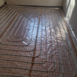 Lidia Turczyn-Bąk - Usługi Hydrauliczno - Budowlane - Układ rur ogrzewania podłogowego na folii izolacyjnej z siatką, widok z góry, surowe wnętrze w trakcie prac wykończeniowych.