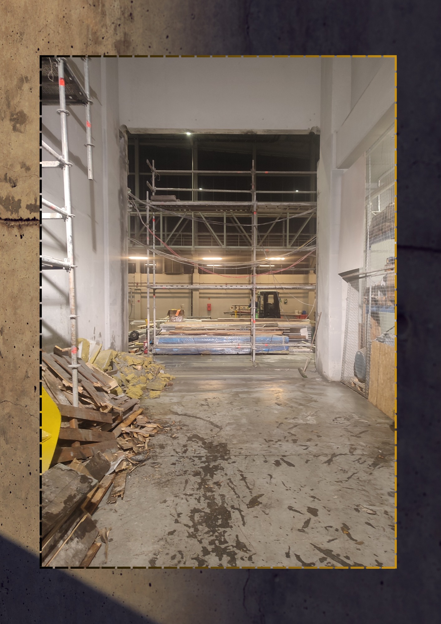 Wnętrze hali w trakcie prac remontowych lub wyburzeniowych; widoczne rusztowania, materiały budowlane zabezpieczone folią, gruz i resztki izolacji na podłodze, oraz w oddali sprzęt budowlany.