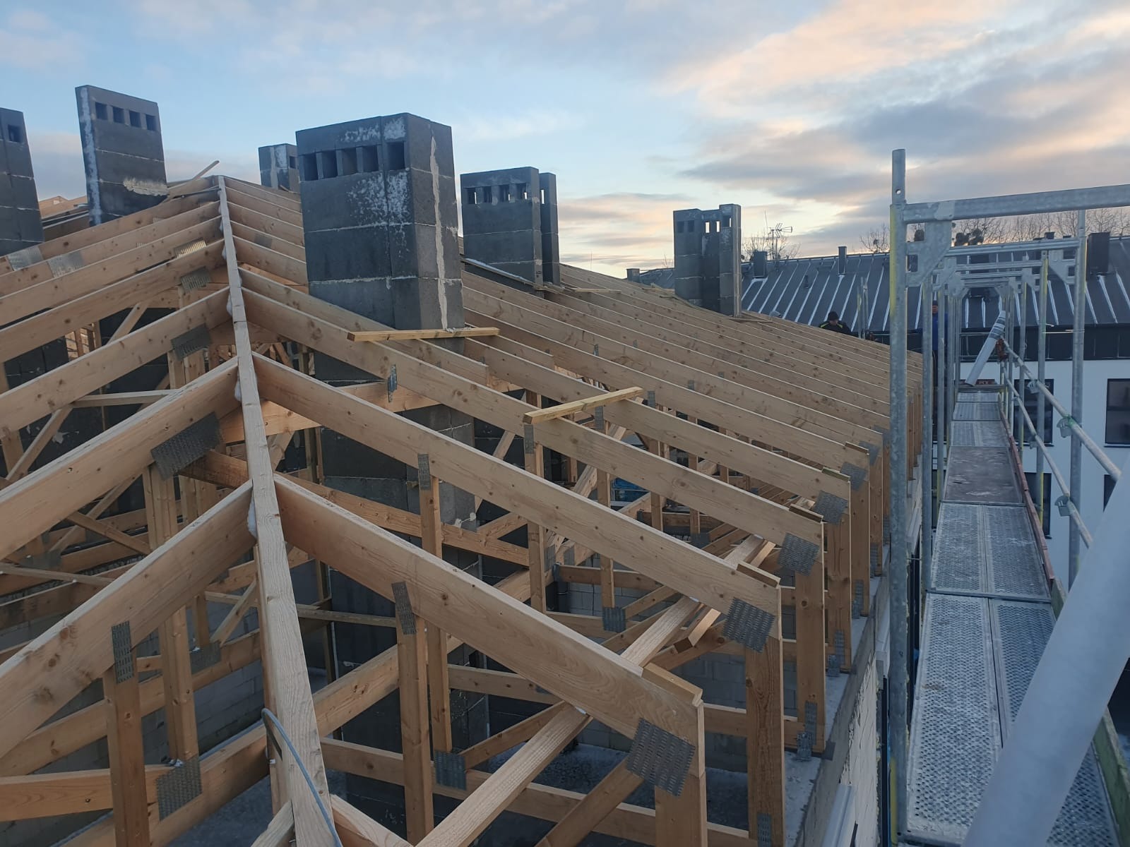 Konstrukcja drewniana dachu z kominami w trakcie budowy w Poznaniu, widok z góry na elementy więźby dachowej i rusztowania.