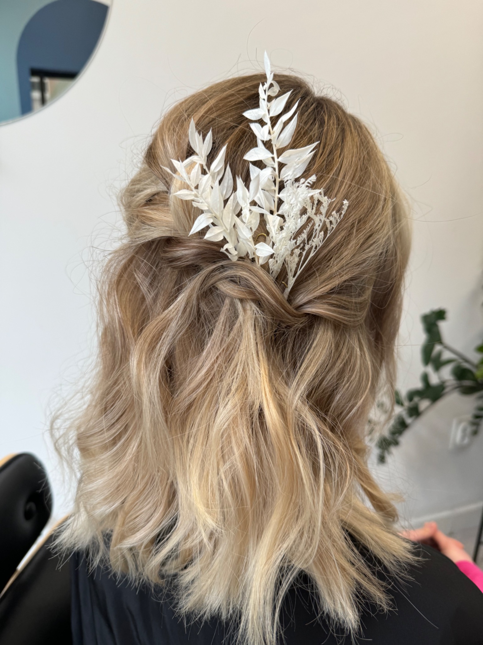 Upięcie blond włosów do ramion z wpiętą białą, delikatną ozdobą z suszonych roślin, widok z tyłu, naturalne światło.