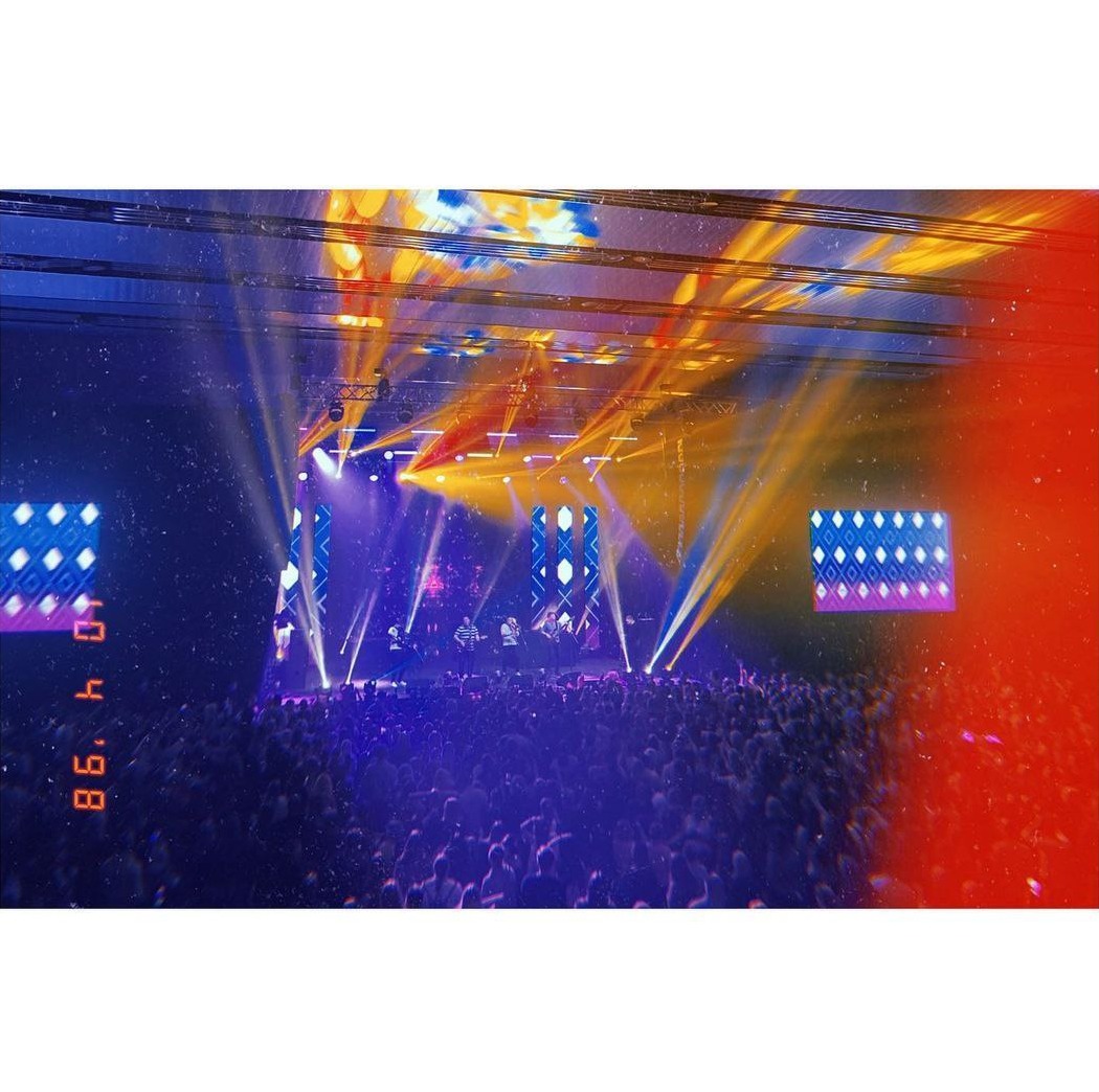 Koncert z widokiem na scenę oświetloną reflektorami i telebimami, tłum ludzi w dole, efekt starego zdjęcia z datą 04.04.86