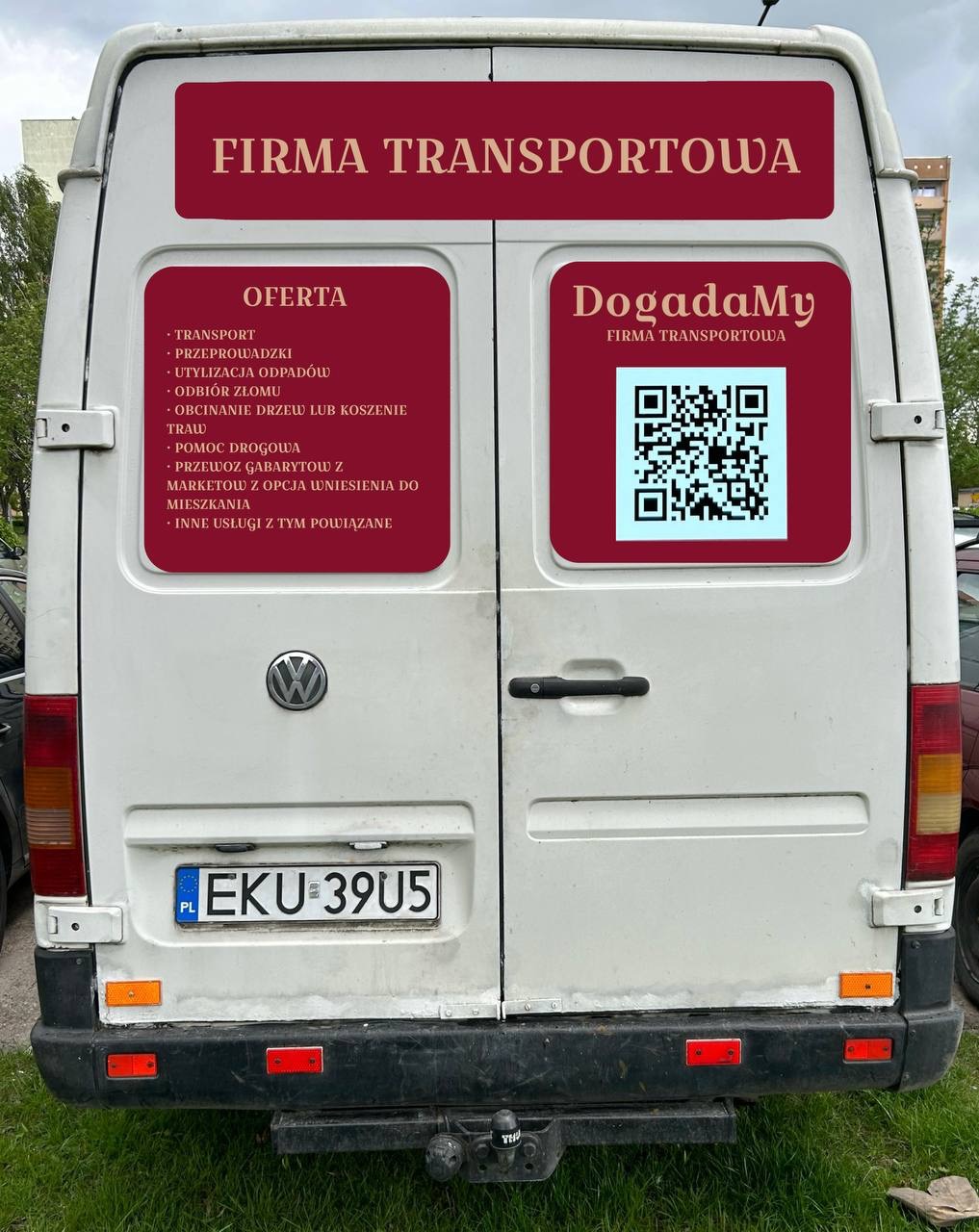 Tył białego furgonetki z naklejkami informującymi o ofercie firmy transportowej, w tym o transporcie, utylizacji odpadów, odbiorze złomu, obcinaniu drzew, pomocy drogowej i przewozie gabarytów...