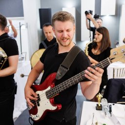Joanna Herliczek - Zespół muzyczny w akcji: basista gra na czerwonej gitarze basowej, obok akordeonista i saksofonistka. W tle perkusista i fotograf. Dekoracja stołu weselnego.