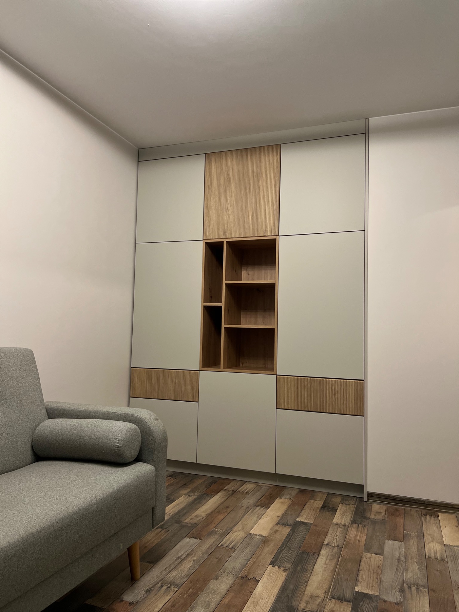 Nowoczesna zabudowa meblowa w salonie z szarym narożnikiem i drewnianą podłogą w stylu vintage.