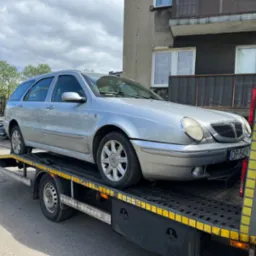 Srebrne kombi Lancia Lybra na lawecie, widoczne tablice rejestracyjne, tło budynku mieszkalnego.