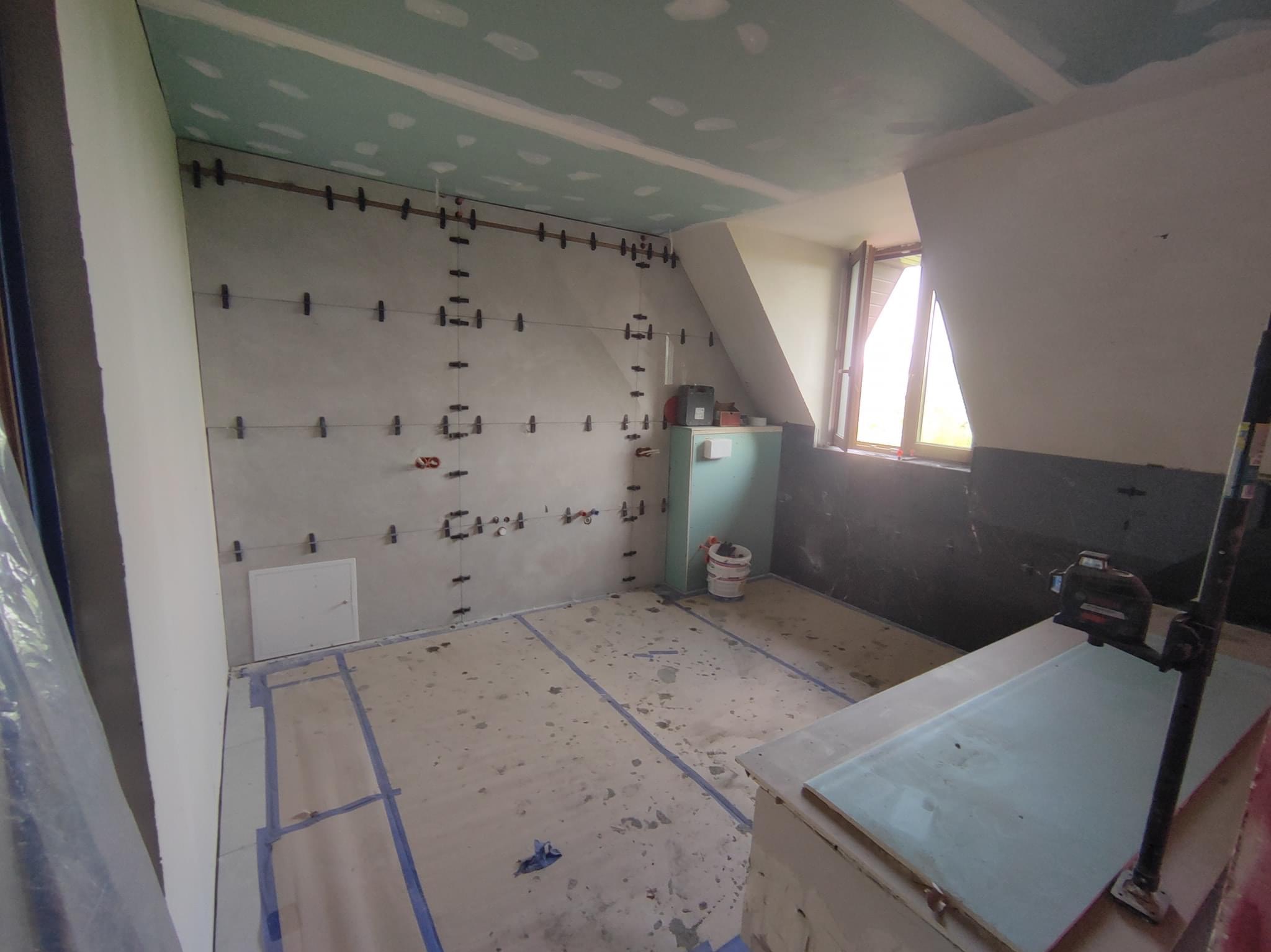 Pokój w trakcie prac wykończeniowych: ściany przygotowane pod gładź z widocznymi listwami i poziomnicą, sufit z płyt kartonowo-gipsowych, zabezpieczona podłoga.