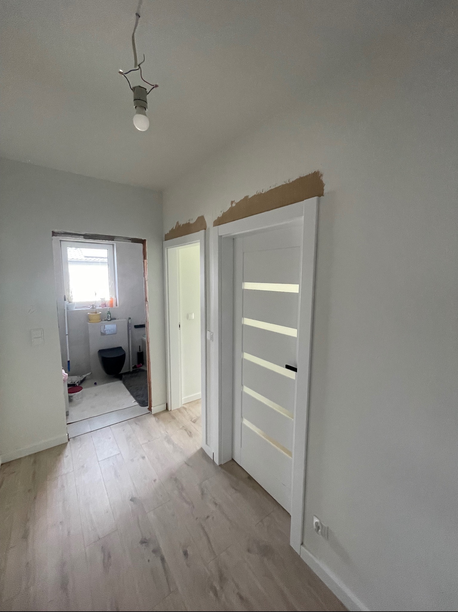 Wnętrze w trakcie remontu: zamontowane białe drzwi z szybami, widoczne fragmenty przygotowanych ścian do malowania, ułożone panele podłogowe w odcieniach szarości.