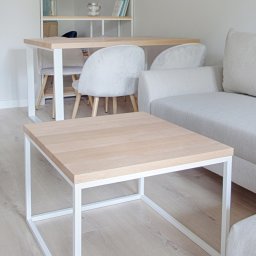 Robim wood - Minimalistyczny stolik kawowy z blatem z jasnego drewna i białą, metalową ramą, na tle salonu z sofą i stołem jadalnym.