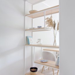 Robim wood - Biały regał z jasnego drewna w minimalistycznym wnętrzu. Dekoracje: wazon z trawami, książki, miseczki, koszyk. Stonowana kolorystyka, nowoczesny design.