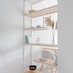 Biały regał z jasnego drewna w minimalistycznym wnętrzu. Dekoracje: wazon z trawami, książki, miseczki, koszyk. Stonowana kolorystyka, nowoczesny design.