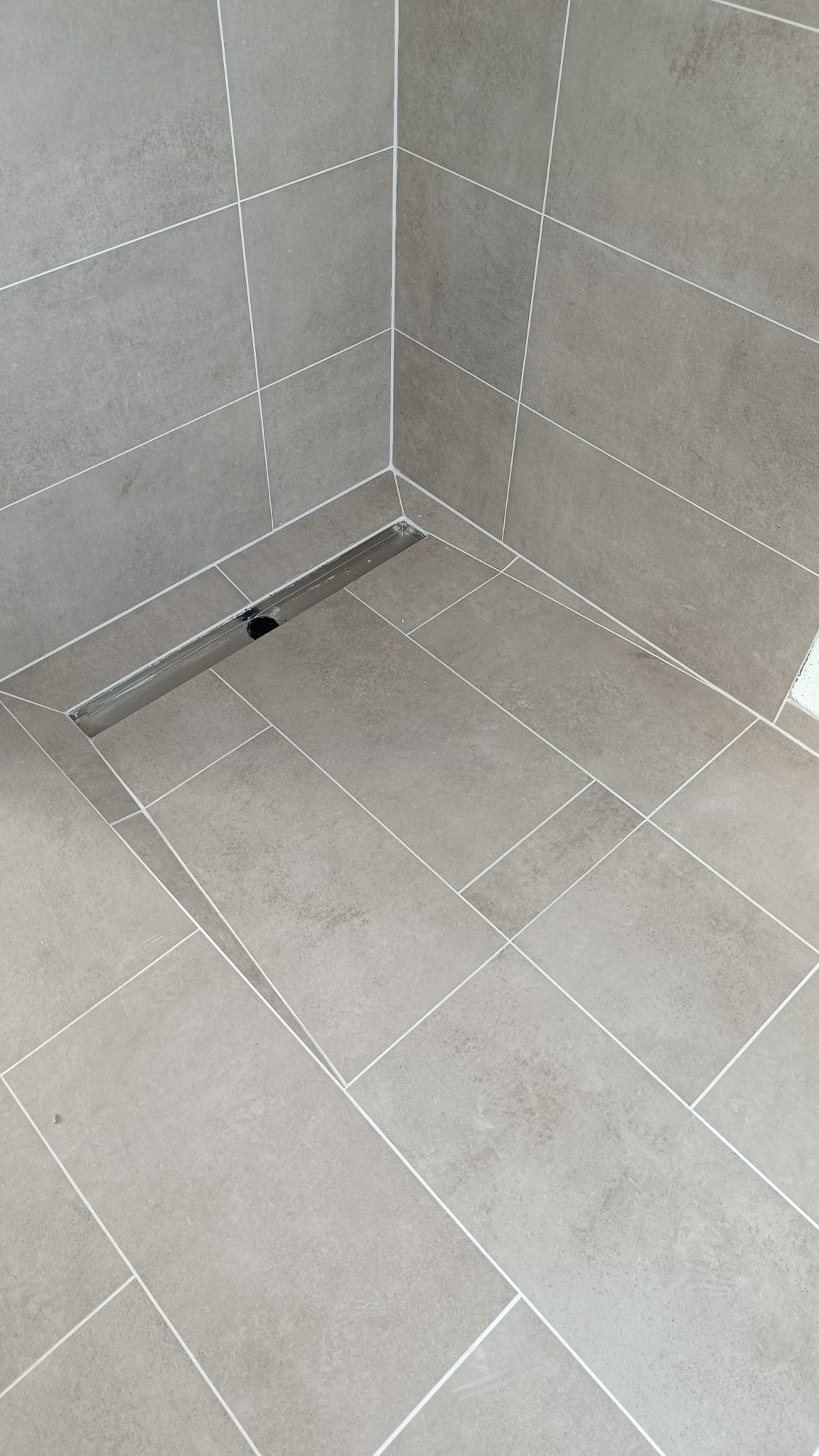 Wykończona kabina prysznicowa z szarymi, prostokątnymi płytkami i liniowym odpływem podłogowym.