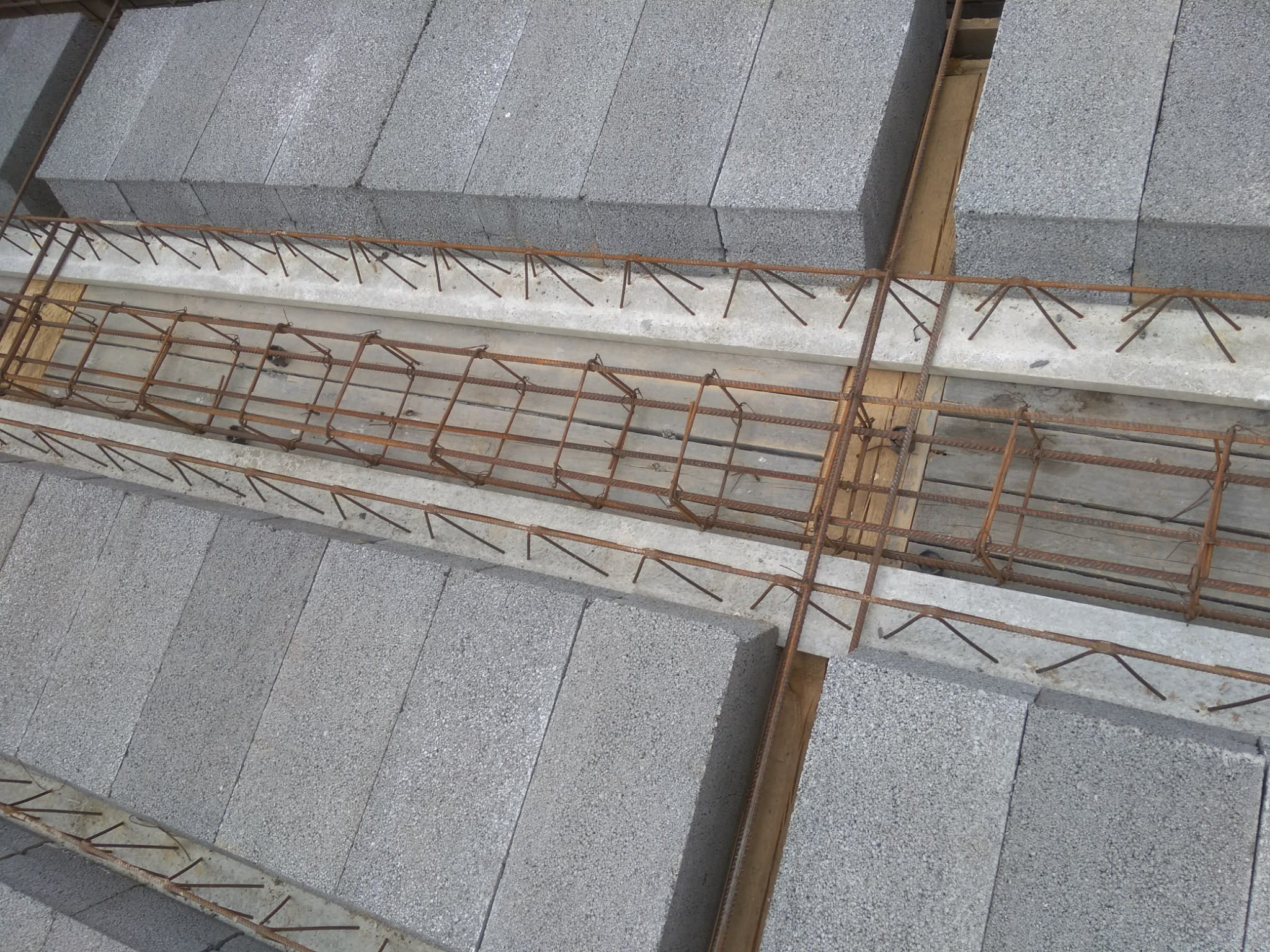 Wieniec żelbetowy w szalunku, zbrojony stalą, pomiędzy warstwami bloczków betonowych na budowie.