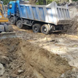 Żółta koparka Liebherr 904 i niebieska wywrotka na placu budowy podczas wykonywania wykopu w ziemi.