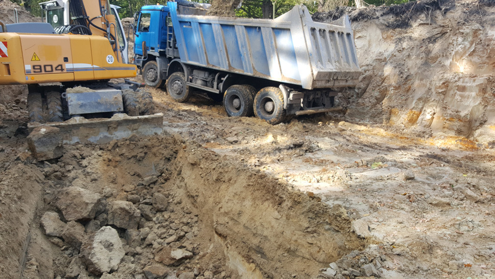 Żółta koparka Liebherr 904 i niebieska wywrotka na placu budowy podczas wykonywania wykopu w ziemi.