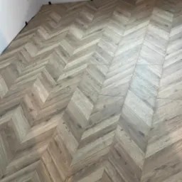 Ułożone panele podłogowe w jodełkę francuską, widok z góry, widoczne listwy przypodłogowe w trakcie montażu i grzejnik na ścianie.