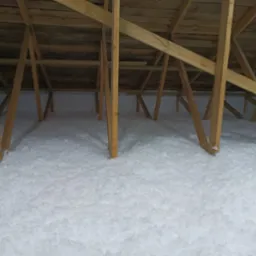 Poddasze z drewnianą konstrukcją wypełnione białą, sypką izolacją, widok z dołu.