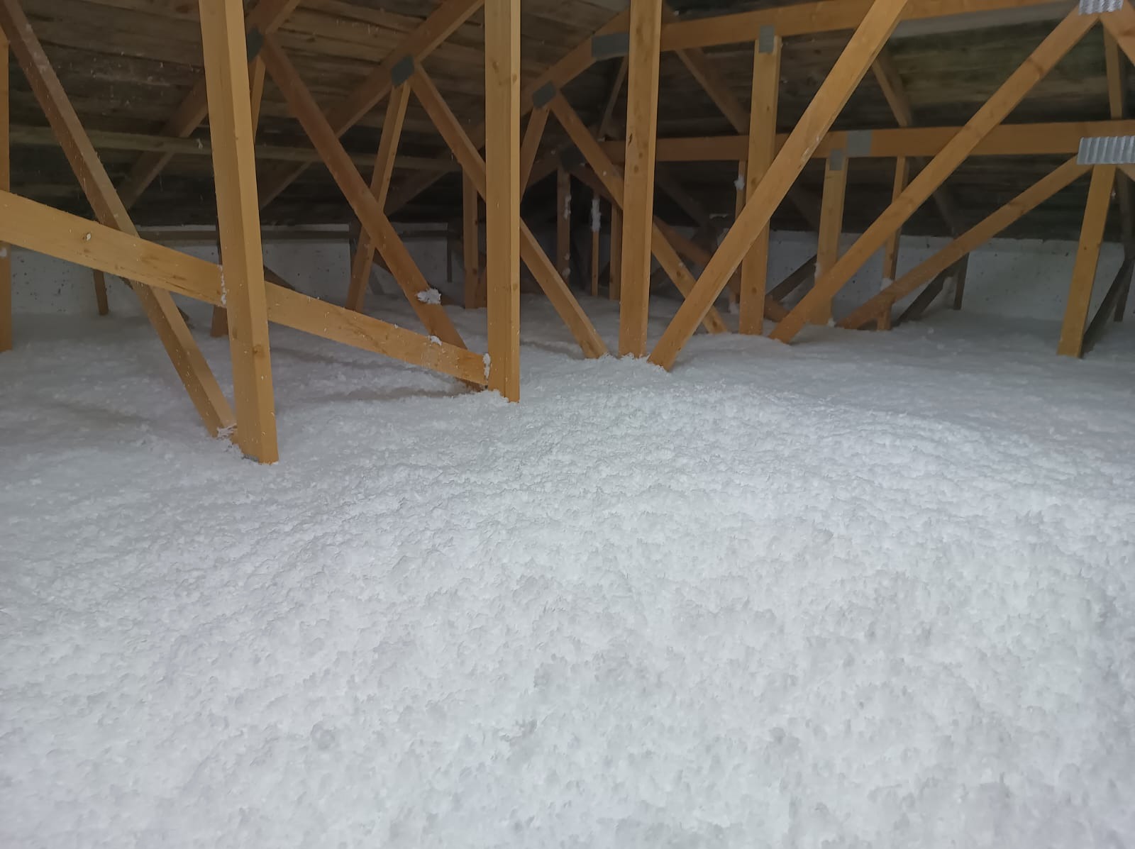 Poddasze z drewnianą konstrukcją wypełnione białą, sypką izolacją, widok z niskiej perspektywy.
