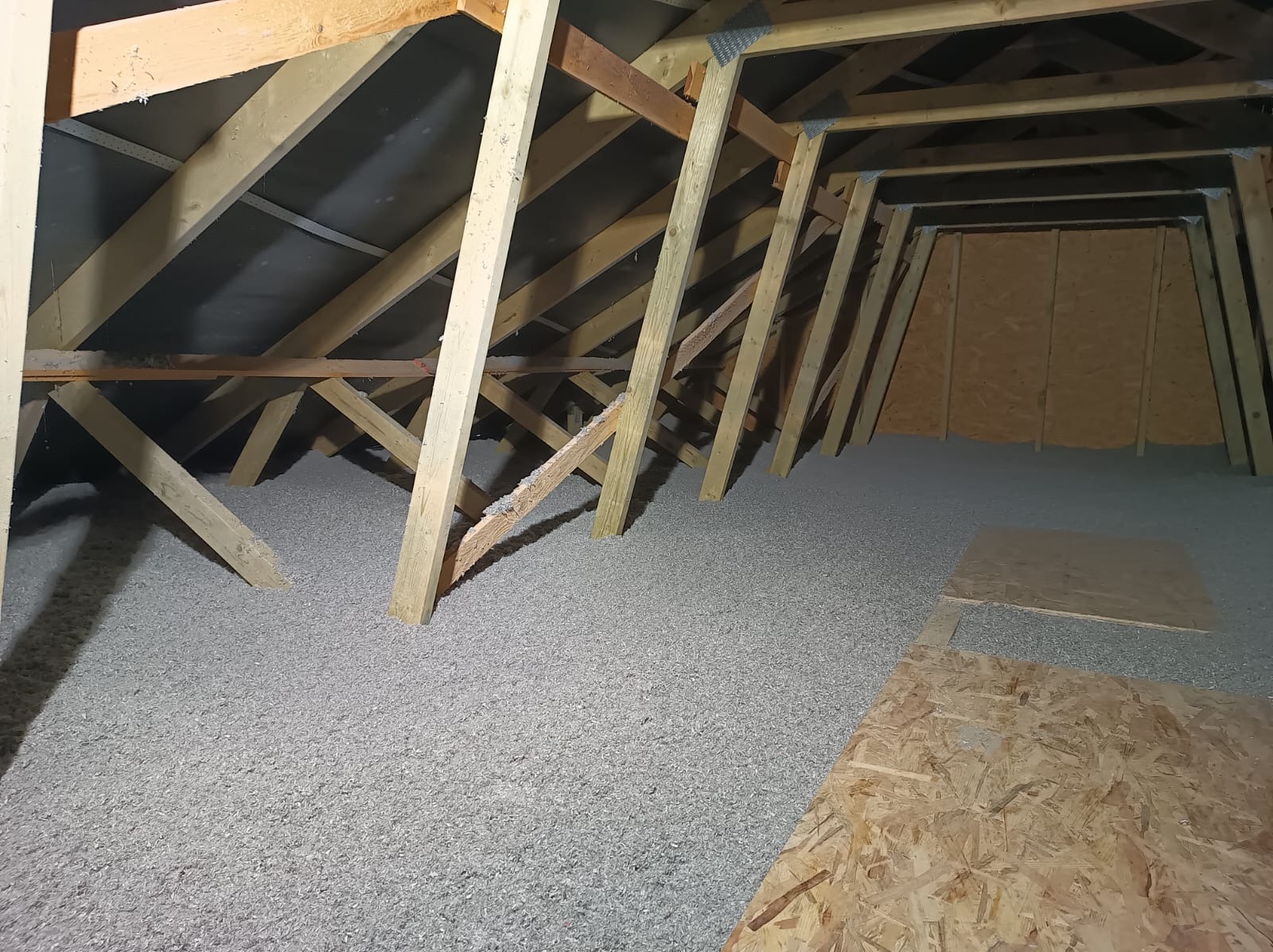 Poddasze w Bełchatowie z drewnianą konstrukcją pokryte szarą warstwą izolacyjną, widoczne płyty OSB.