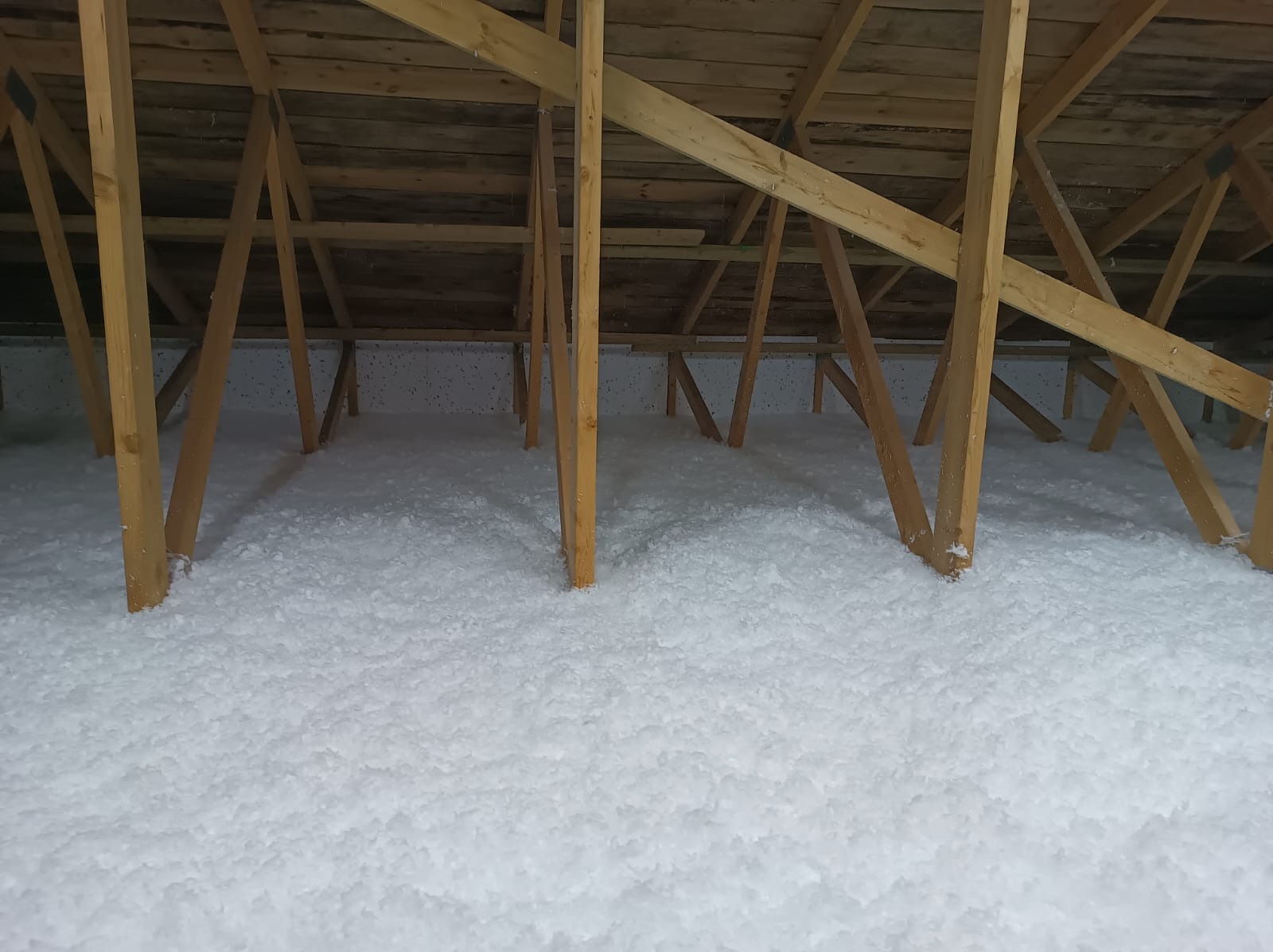 Poddasze z drewnianą konstrukcją wypełnione białą, sypką izolacją, widok z dołu.