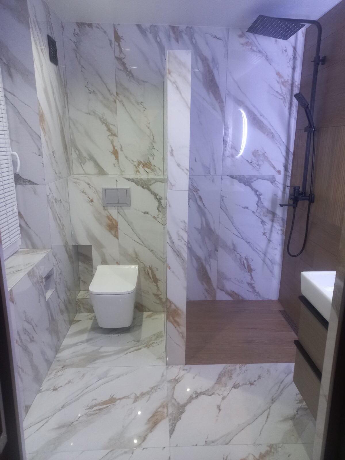 Nowoczesna łazienka z marmurowymi płytkami, wiszącą toaletą i czarną armaturą prysznicową.