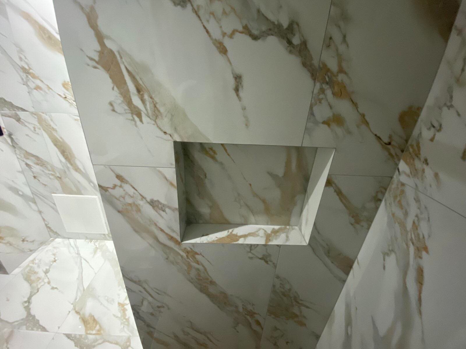 Wnęka w ścianie wyłożonej białymi płytkami imitującymi marmur z brązowymi żyłami, widok z dołu.
