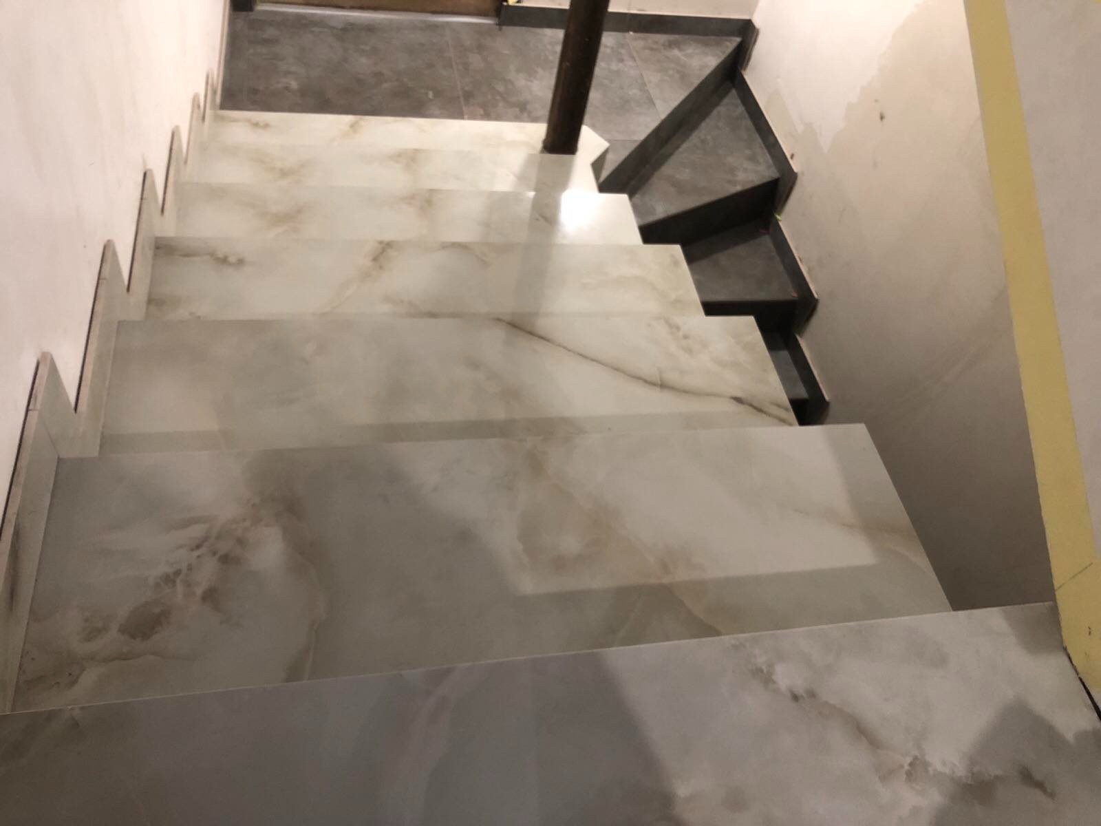 Wykończone marmurowe schody wewnętrzne w trakcie remontu w Warszawie, widok z góry, z fragmentem czarnych schodów na górze i żółtą taśmą malarską na ścianie.
