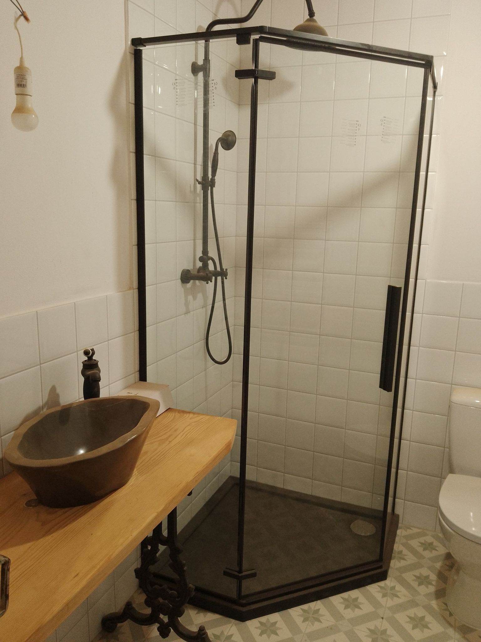 Nowoczesna łazienka z kabiną prysznicową w czarnej ramie, umywalką w stylu retro na drewnianym blacie i geometrycznymi płytkami podłogowymi.