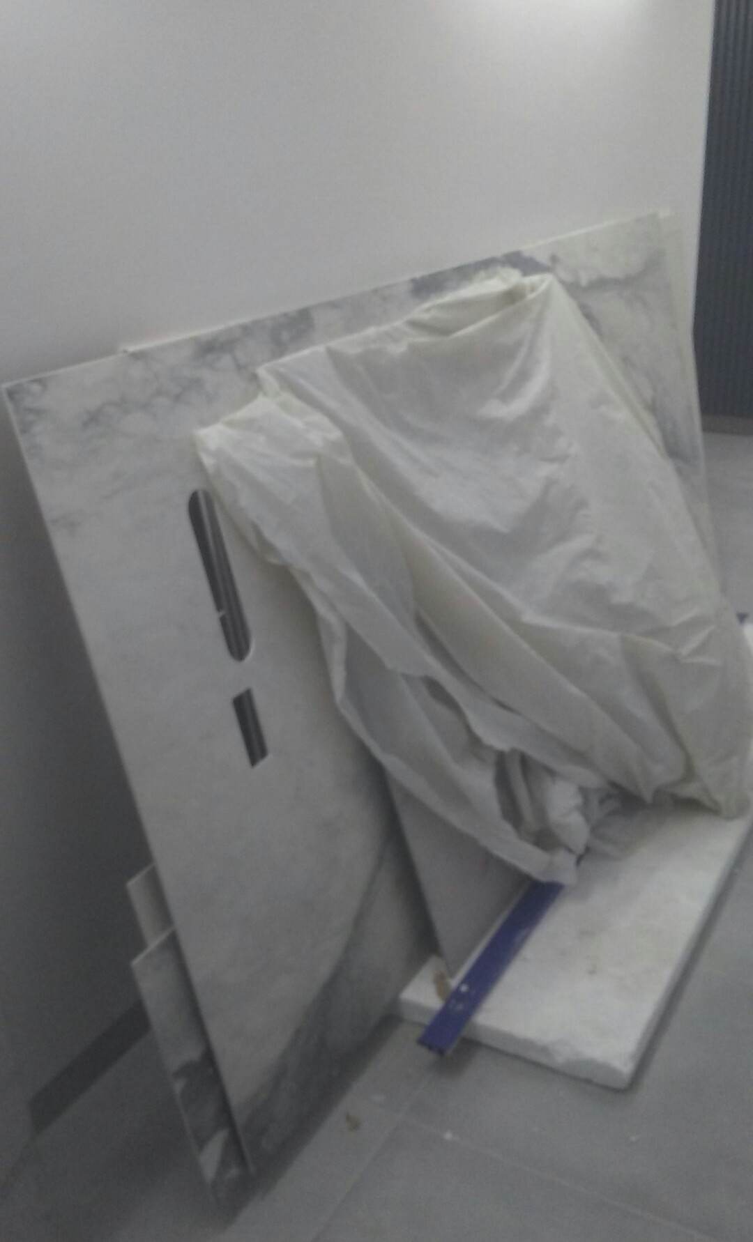 Płyty marmurowe z wyciętymi otworami, częściowo przykryte folią ochronną, opierają się o ścianę w pomieszczeniu w trakcie prac wykończeniowych.