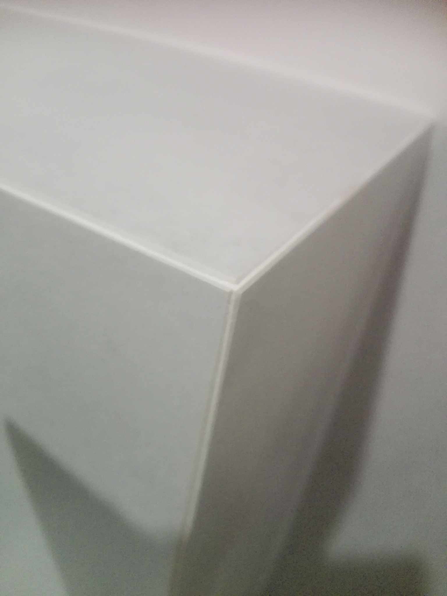 Fragment białej ściany z płyt kartonowo-gipsowych, widoczny narożnik i łączenie płyt, delikatne cieniowanie.