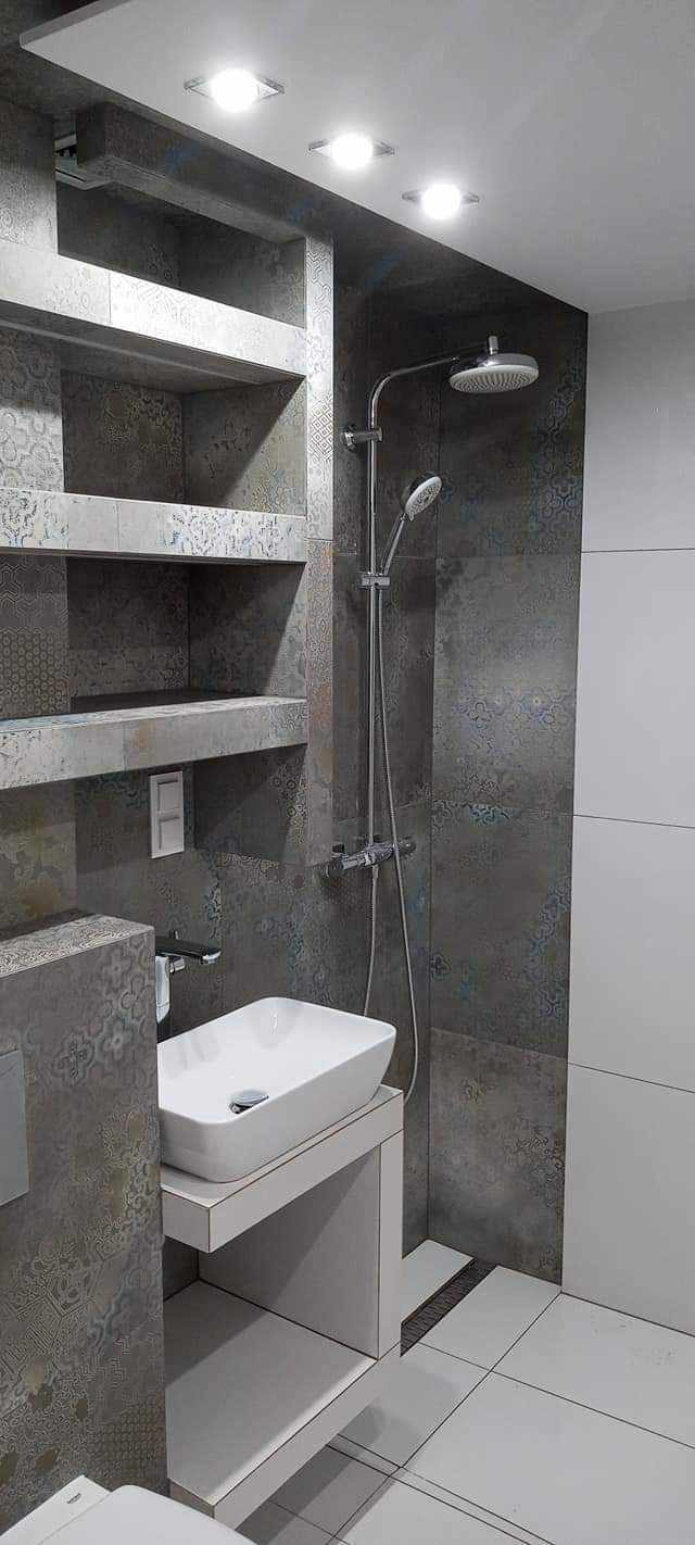 Nowoczesna łazienka z szarymi, wzorzystymi płytkami, białą umywalką nablatową i wnękami z półkami, oświetlenie punktowe w suficie.