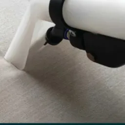 Dysza odkurzacza piorącego, z widocznymi elementami mocującymi, przykładana do jasnej, tekstylnej powierzchni, prawdopodobnie dywanu lub tapicerki.