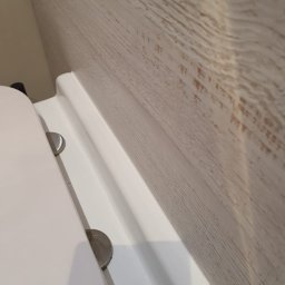 Salvare Serwis - Fragment toalety z widocznym białym sedesem i fragmentem ściany pokrytej panelami imitującymi jasne drewno, z wyraźną białą listwą przypodłogową.