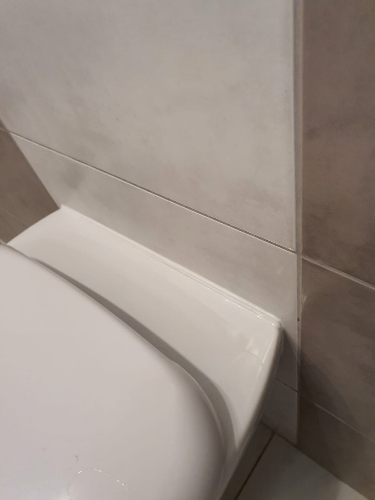 Szczelne połączenie silikonowe między białą ceramiką sanitarną a szarą płytką w łazience w Gdańsku, świeżo po uszczelnieniu.