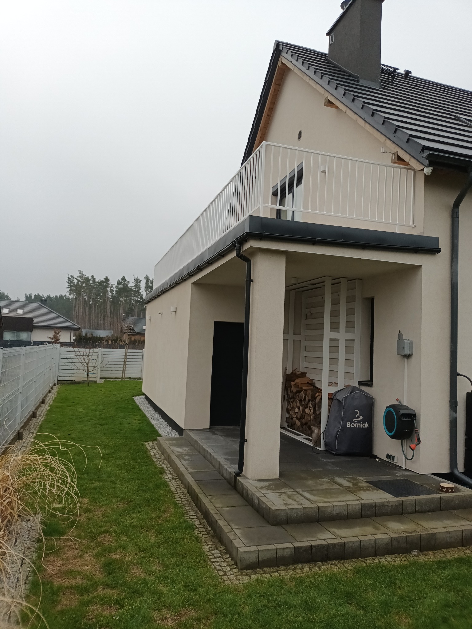 Nowoczesny dom w Kowalu z balkonem zabezpieczonym białą, metalową balustradą, widok z zewnątrz na zadbany trawnik i ogrodzenie.