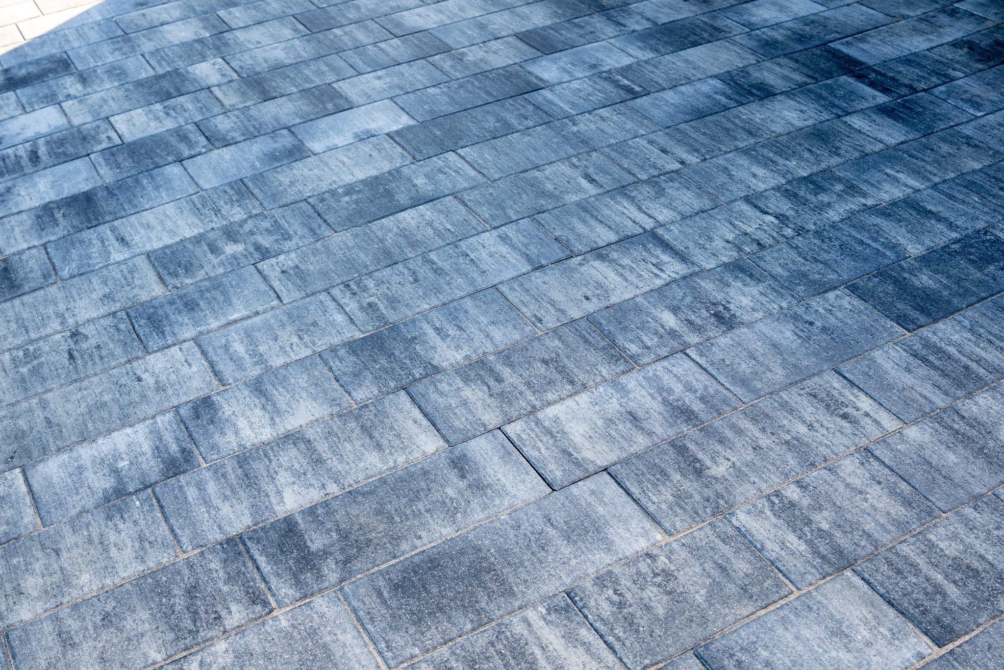 Ułożona, szaro-niebieska kostka brukowa w kształcie prostokątów, ułożona pod kątem, z widoczną fakturą i drobnymi szczelinami wypełnionymi piaskiem.