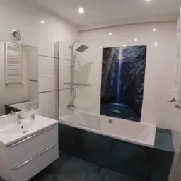 Nowoczesna łazienka z białą armaturą, płytkami imitującymi wodospad nad wanną oraz turkusową podłogą i obudową wanny.