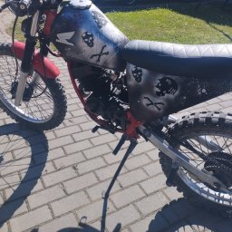 Zrób to sam - Motocykl Honda z niestandardowym malowaniem czaszek i kości na zbiorniku, stojący na kostce brukowej.