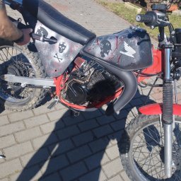Zrób to sam - Motocykl Honda z customowym malowaniem czaszek i czerwonych plam, stojący na brukowanym podłożu, widoczne opony terenowe i czerwona rama.